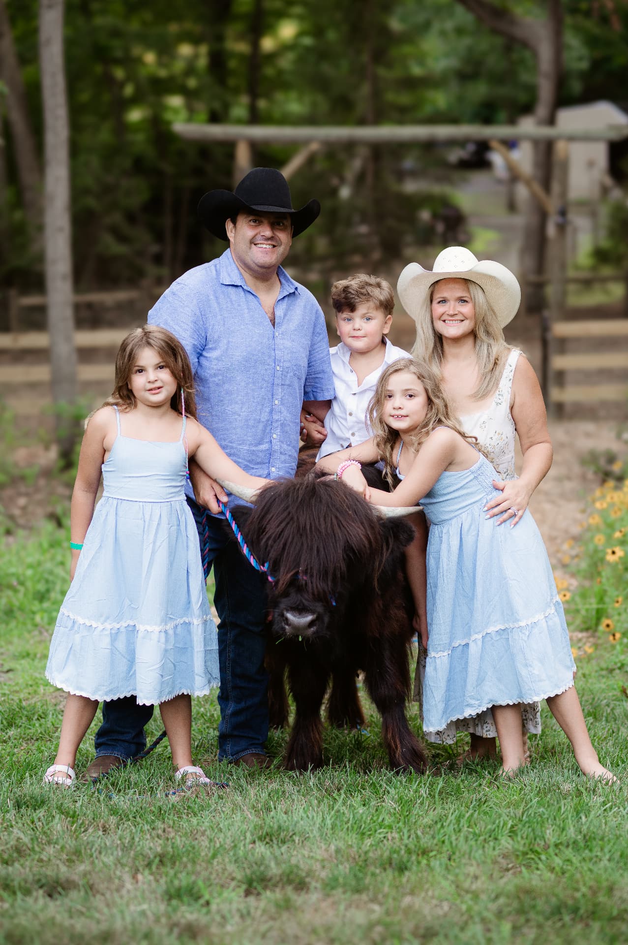 A smiling family in cowboy hats with their Highland cow